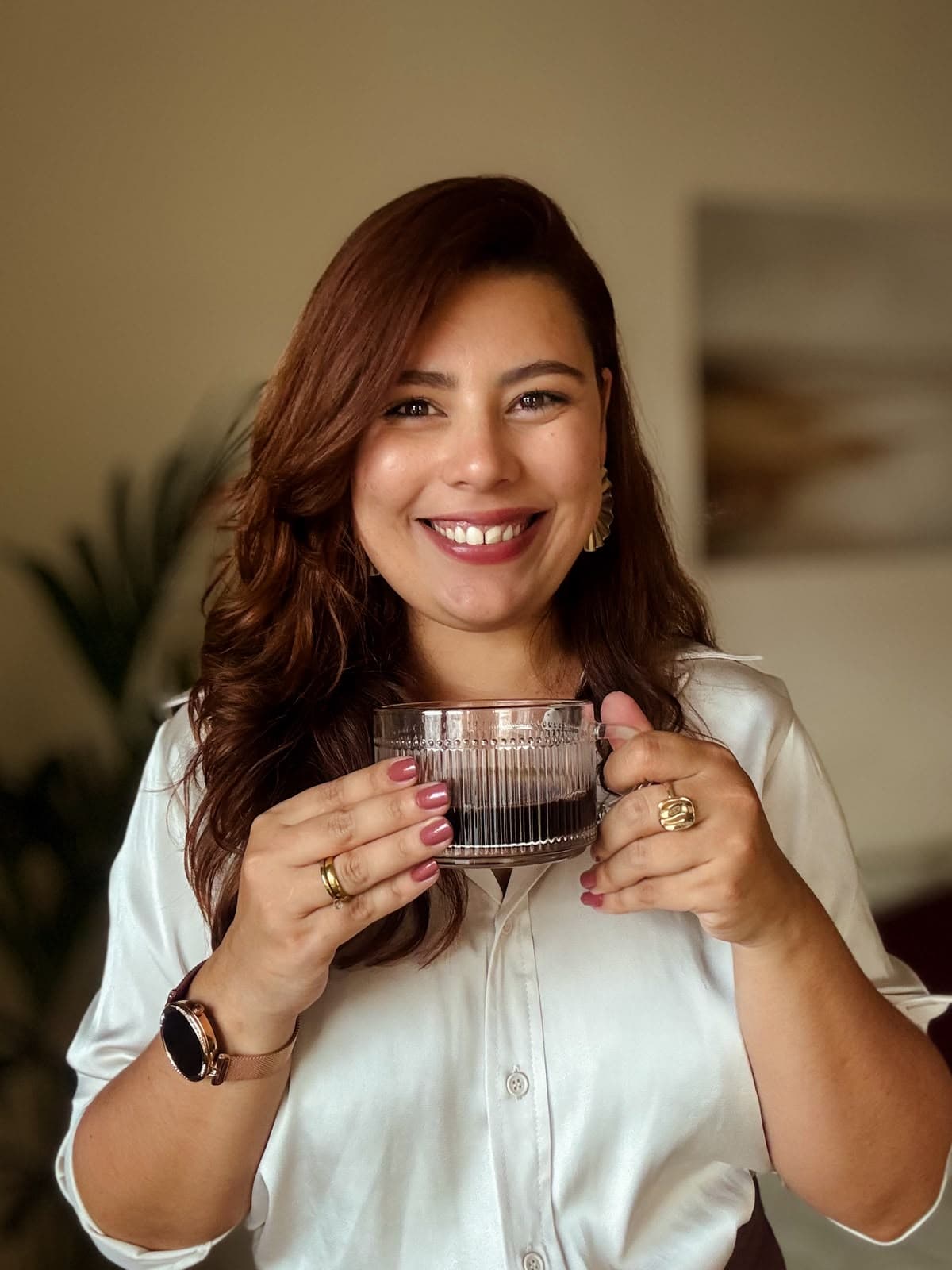 Taynara Oliveira sorrindo, segurando uma xícara em um ambiente acolhedor.